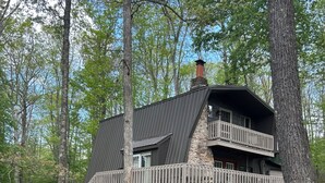 A two-story cabin with a stone foundation, a metal roof, and a wooden deck.