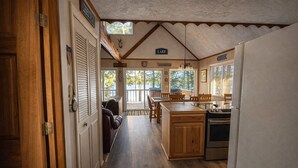 A kitchen with wooden cabinets, a stove, and a dining area with a table and chairs. - Sunset Beach Chalet with Hot Tub & Fire Pit Near Hiking, Skiing & Snowmobiling (Gaylord)