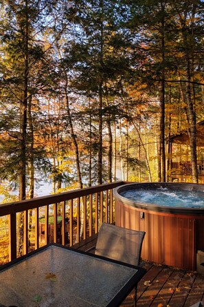 A hot tub on a wooden deck with a view of a forest and a body of water.