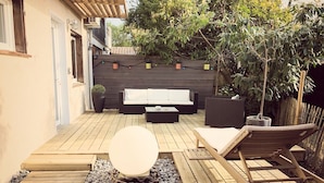 Un pontile in legno con un tavolo rotondo bianco, una poltrona da lounge in legno e un divano.