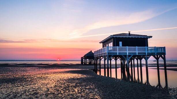 Un molo si protende su acque calme al tramonto, con un edificio in legno all'estremità.