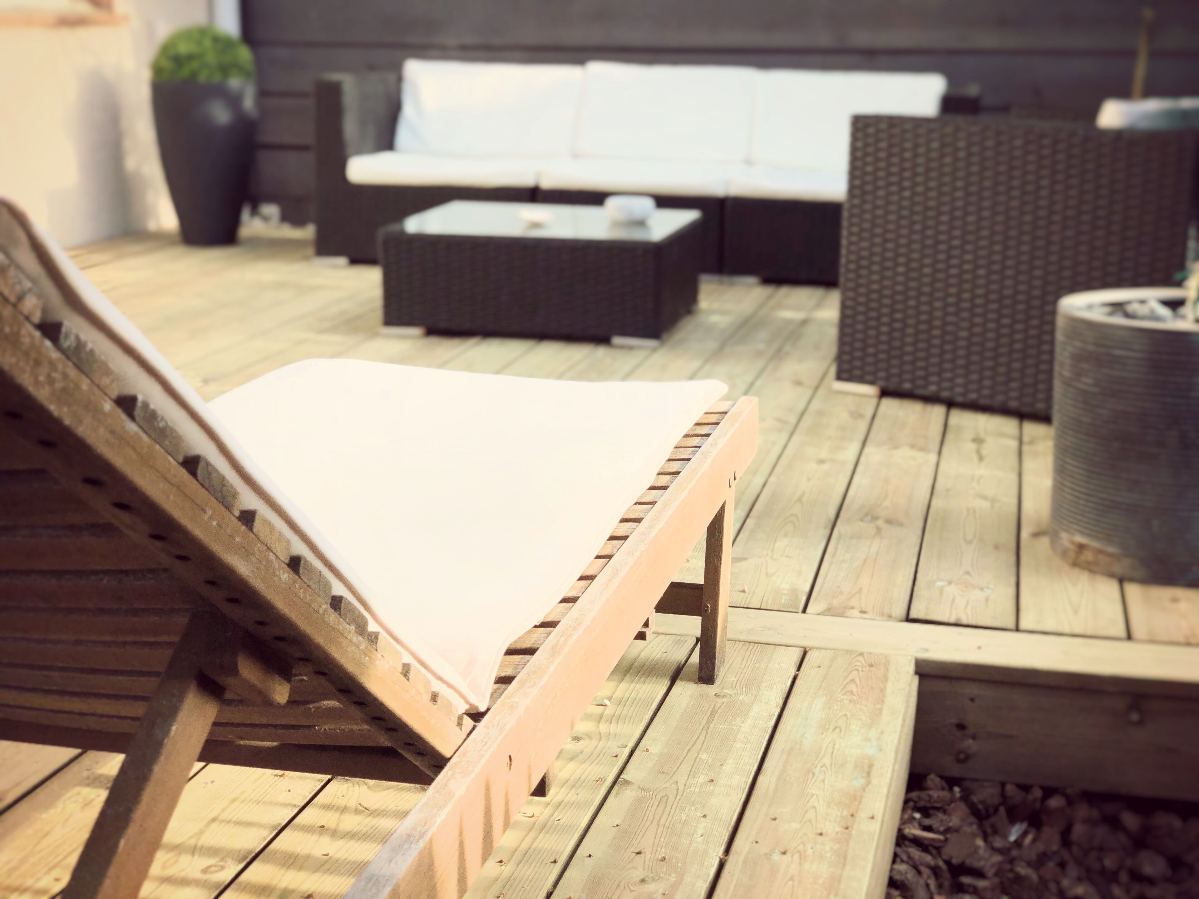 Una terraza de madera con una silla de descanso, un sofá y una mesita.