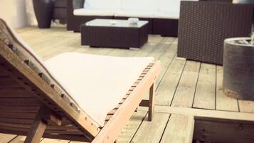 Una terraza de madera con una silla de descanso, un sofá y una mesita.