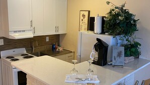 A kitchen with white cabinets, a stove, a refrigerator, a sink, and a bar area with stools. - BEST DEALS NOW !AMAZING BEACH, PRIVACY, UNWIND. SLEEP 4, FREE CHAIRS, BBQ, PKG  (Madeira Beach)