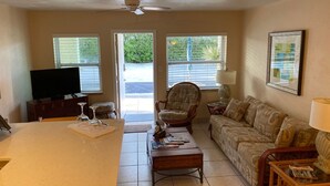 A living room with a television, a coffee table, a sofa, and a chair. There are windows with blinds, a ceiling fan, and a door leading outside. - BEST DEALS NOW !AMAZING BEACH, PRIVACY, UNWIND. SLEEP 4, FREE CHAIRS, BBQ, PKG  (Madeira Beach)
