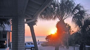 A sunset view from a balcony with palm trees and a parked car. - BEST DEALS NOW !AMAZING BEACH, PRIVACY, UNWIND. SLEEP 4, FREE CHAIRS, BBQ, PKG  (Madeira Beach)