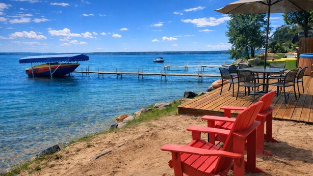 Una terraza frente al mar con sillas Adirondack rojas, una mesa de madera y vista al agua con barcos.