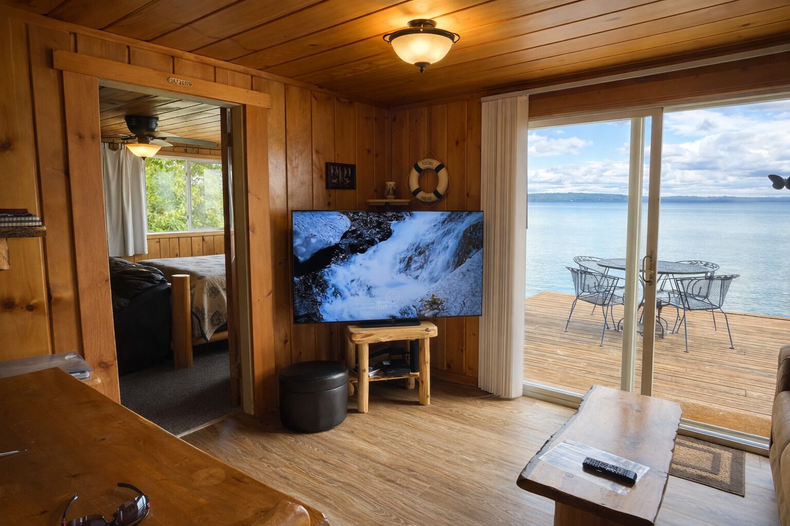 A wooden cabin interior with a TV, wooden furniture, a balcony with a view of the water.