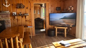 Un interior de madera con una zona de bar, un televisor mostrando una escena de playa y una chimenea.