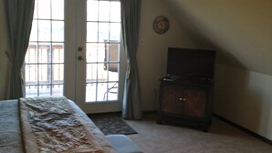Un dormitorio con cama, ventilador de techo, televisor y ventana con cortinas.