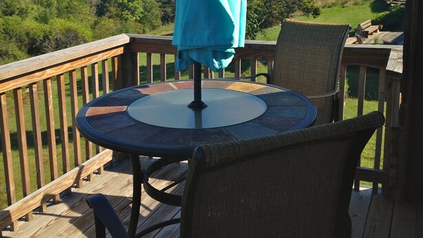 Una terraza de madera con una mesa redonda y sillas, un paraguas y vistas a un paisaje verde.