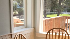 A dining table with chairs, a patterned tablecloth, and a window with a view of a wooden deck and greenery. - BRIGHT! 1.5 Blocks to Beach - Light Filled House (3 Bedroom Plus Den)  (Seaside)