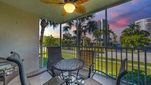 A balcony with a table and chairs, a ceiling fan, and a view of a street with palm trees and buildings.