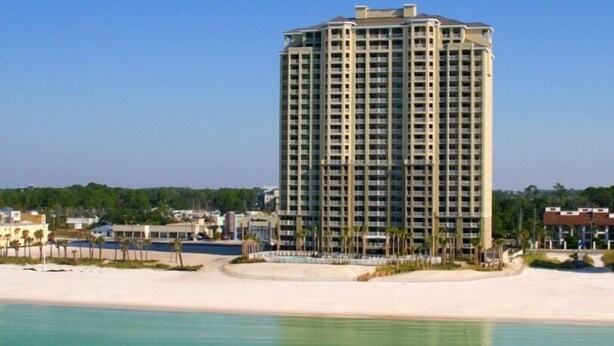 Un hotel di grandi dimensioni con numerose storie, una spiaggia in primo piano e un cielo sereno.