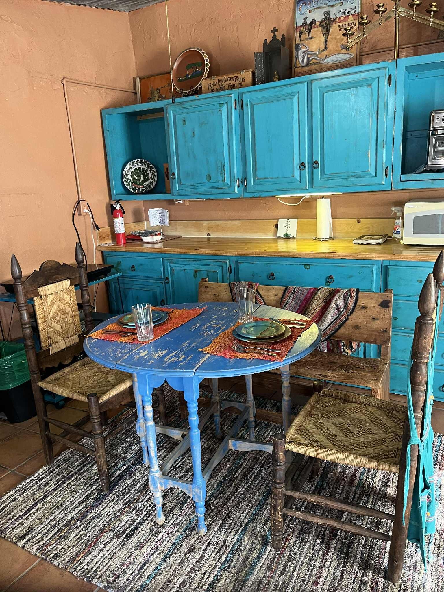 Una cocina con armarios turquesa, una mesa redonda con mantel colorido y un microondas.