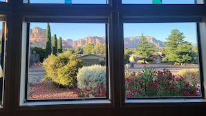 A view through a window with a mountain landscape, including a tall tree and a building with a red roof. - BEST VIEWS! Sleeps 8 Balcony, Firepit, Lawn, Patio, Wildlife (Sedona)
