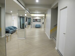 A hallway with a blue sofa, a glass partition, and a staircase. - Suvarnabhumi Oriental Resort (Bangkok)