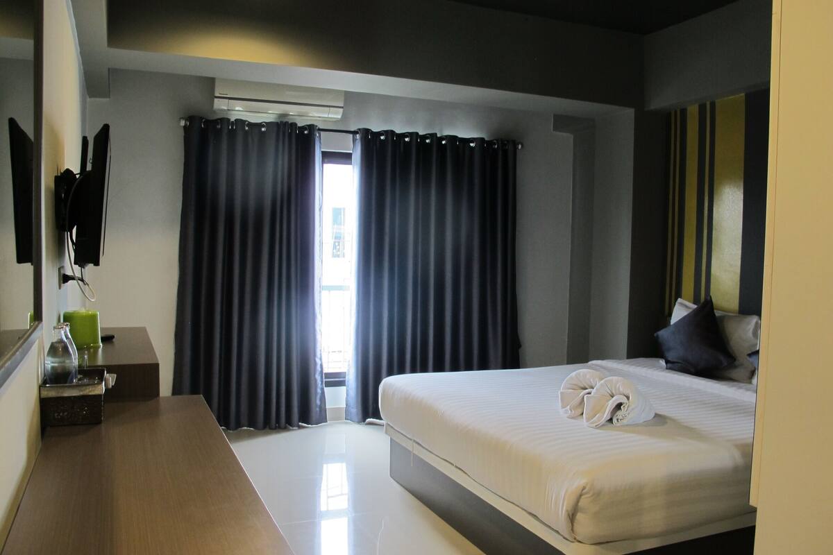 A hotel room with a bed, a bedside table, a mirror, and a window with curtains.