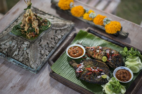 A table with a decorative tray, a carved wooden box, grilled fish, and a bowl of sauce.