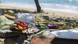 Ein Strandpicknick mit Tisch, Früchten, Blumen und einer Champagnerflasche.