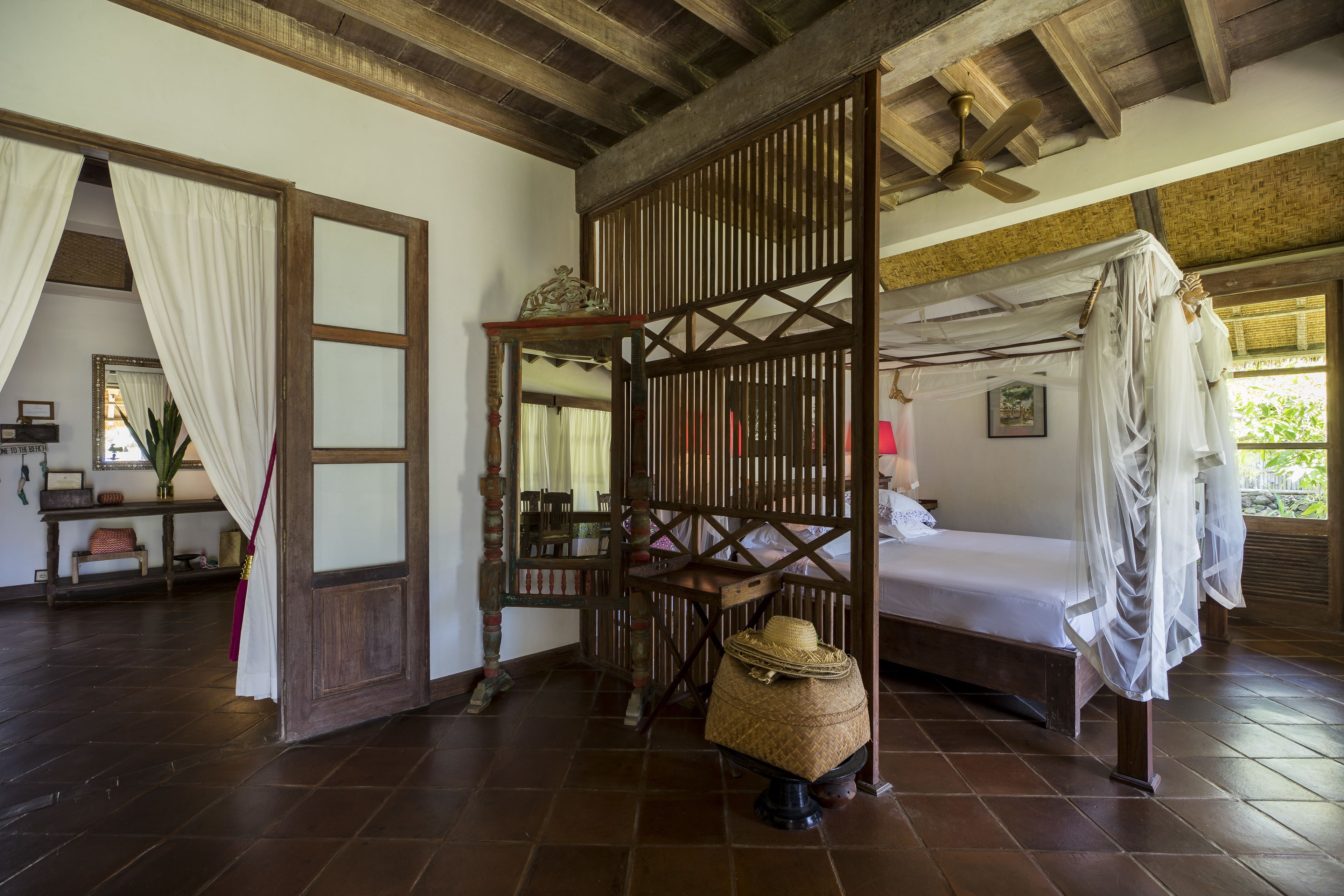 A traditional room with a bed, a wooden partition, a ceiling fan, and a woven basket.