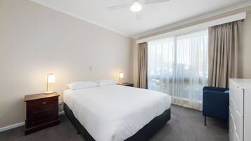 Habitación de hotel con una cama grande, dos lámparas de noche, ventilador de techo, vistas al exterior a través de una ventana y un escritorio con silla.