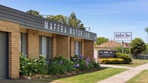 A Motor Inn building with a brick facade, large windows, and a well-maintained garden with various plants and flowers.