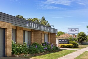 A Motor Inn building with a brick facade, large windows, and a well-maintained garden with various plants and flowers.