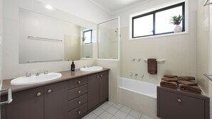 A modern bathroom with two sinks, a large mirror, a bathtub, and a window with a plant.