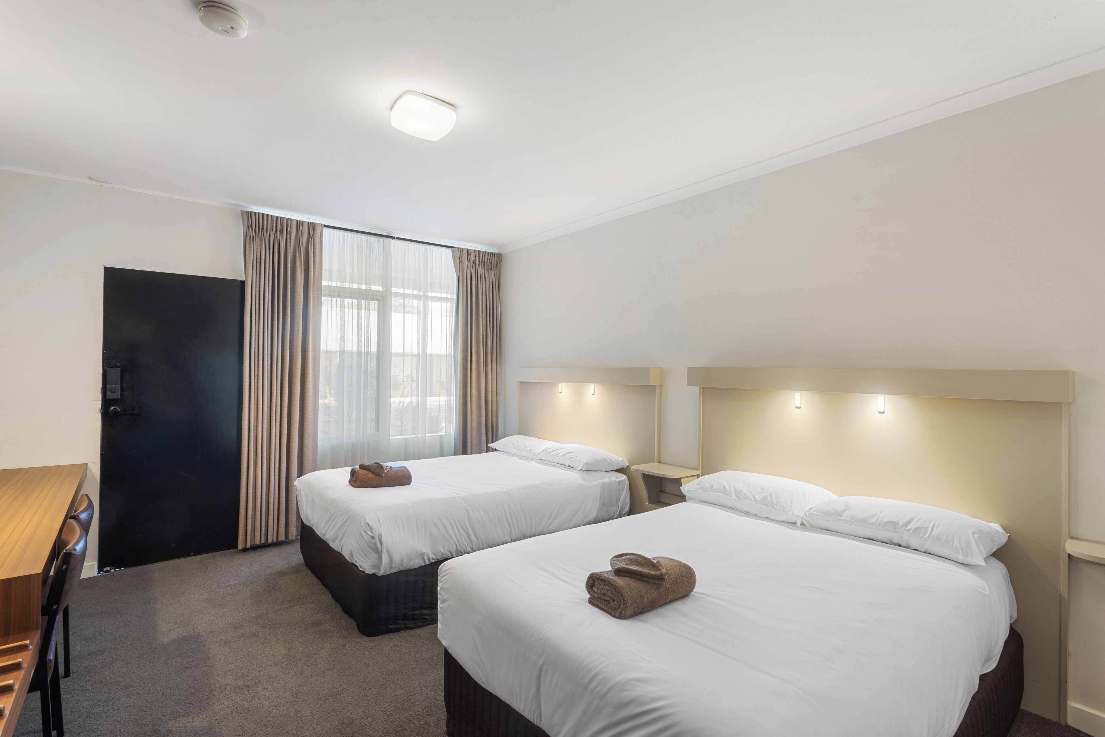 Habitación de hotel con dos camas, un escritorio y una ventana con cortinas.