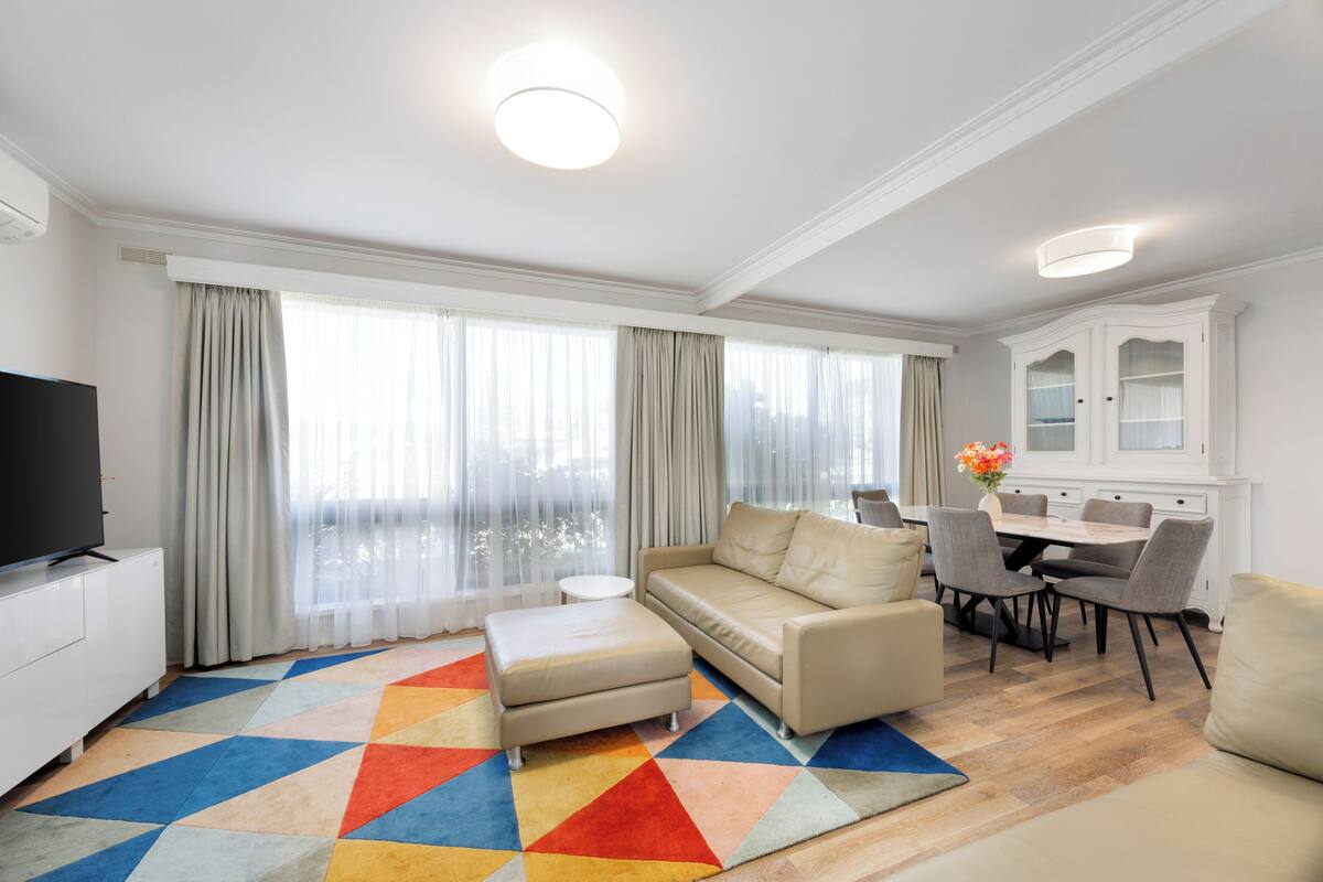 Una sala moderna con un sofá color beige, una mesa de centro y un comedor con un armario blanco y sillas.