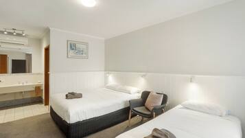 A hotel room with two beds, a bathroom with a sink and mirror, and a painting on the wall.