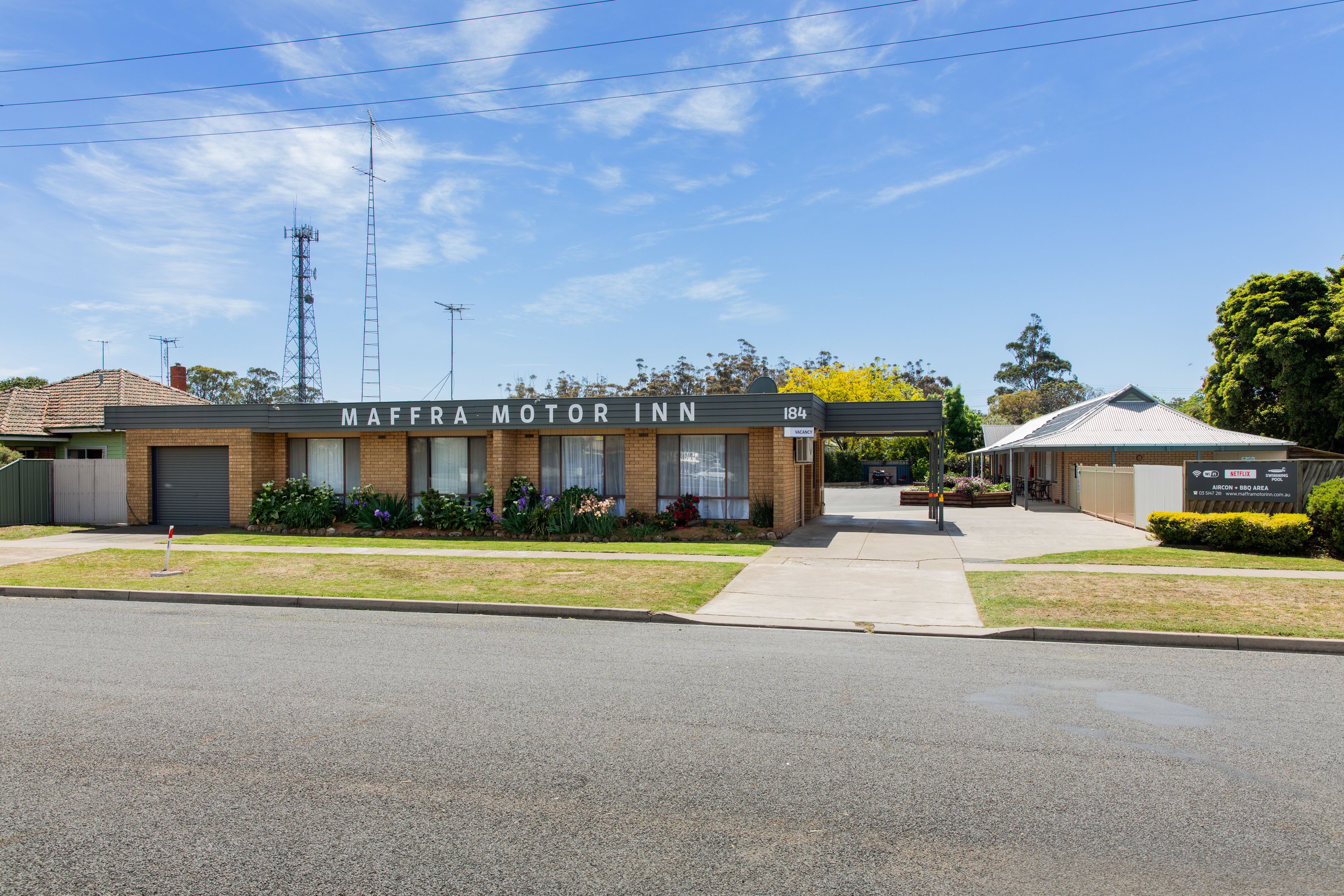 A building labeled "MAFFRA MOTOR INN" with a brick facade, a covered entrance, and a small garden area with flowers.