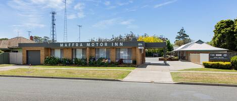 A building labeled "MAFFRA MOTOR INN" with a brick facade, a covered entrance, and a small garden area with flowers.