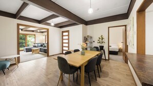 Habitación amplia con una mesa de madera, sillas y un ventanal grande. Se observa un sofá y una pequeña mesa al fondo.