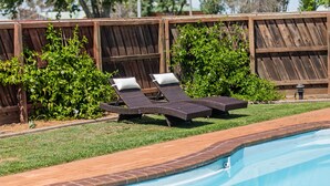 A swimming pool with two sun loungers and a wooden fence in the background.