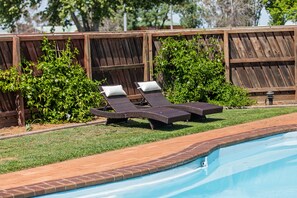 A swimming pool with two sun loungers and a wooden fence in the background.