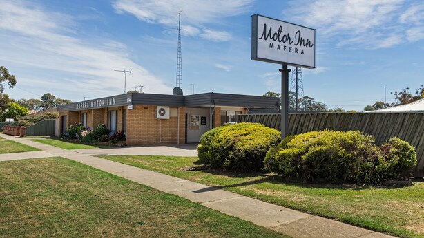 A Motor Inn building with a sign, a satellite dish, and a fenced area with bushes.