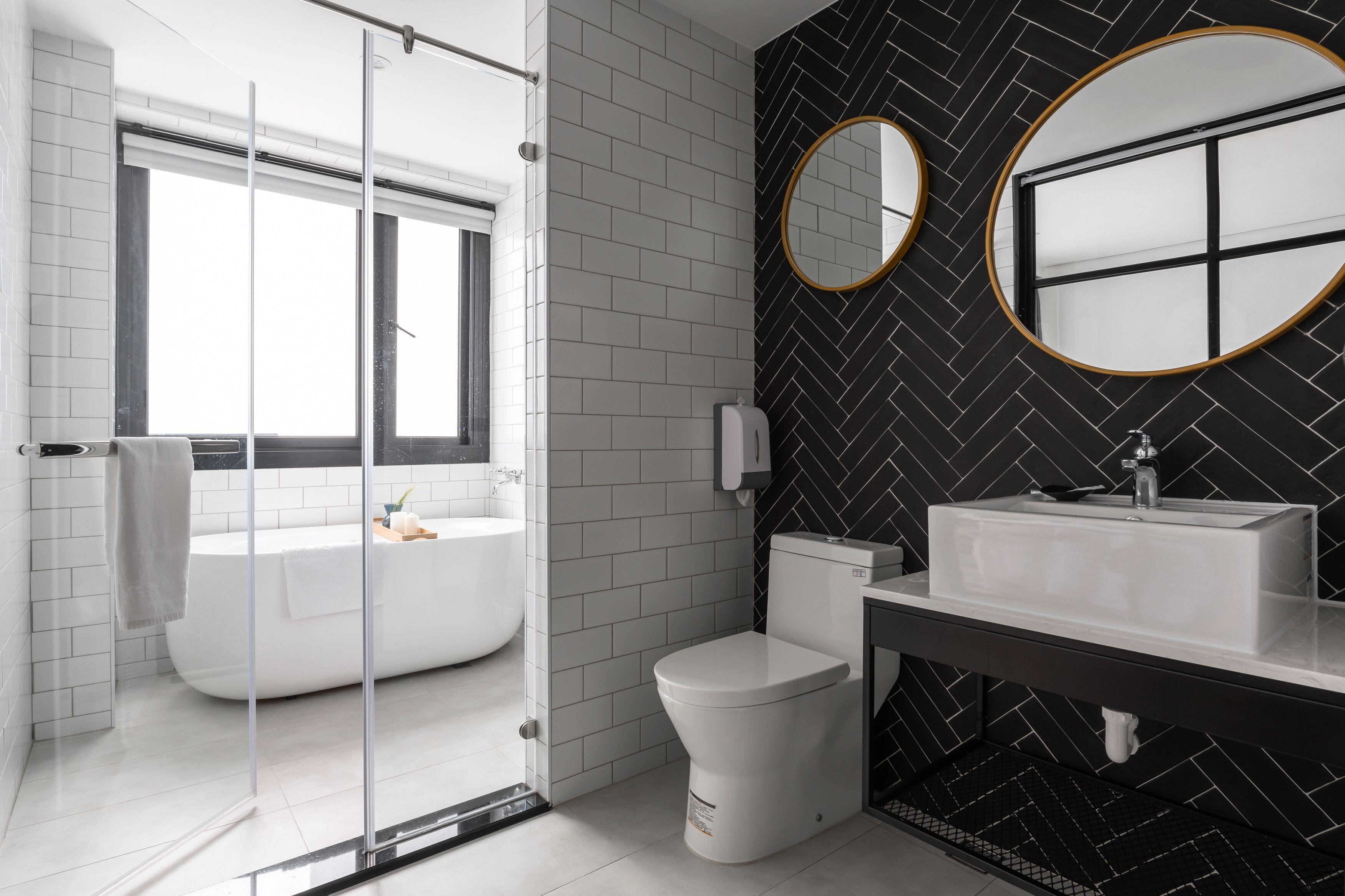 A modern bathroom with a glass shower enclosure, a white bathtub, a toilet, and a vanity with a sink and two round mirrors.