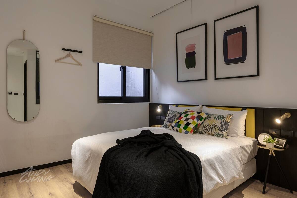 Een moderne slaapkamer met een bed, nachtkastje, spiegel en twee kunstwerken in lijsten aan de muur.