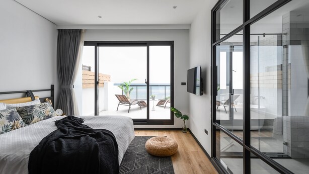 A modern bedroom with a large bed, a TV, and a balcony with a view of the sea. - Hido Hotel I (Hengchun)