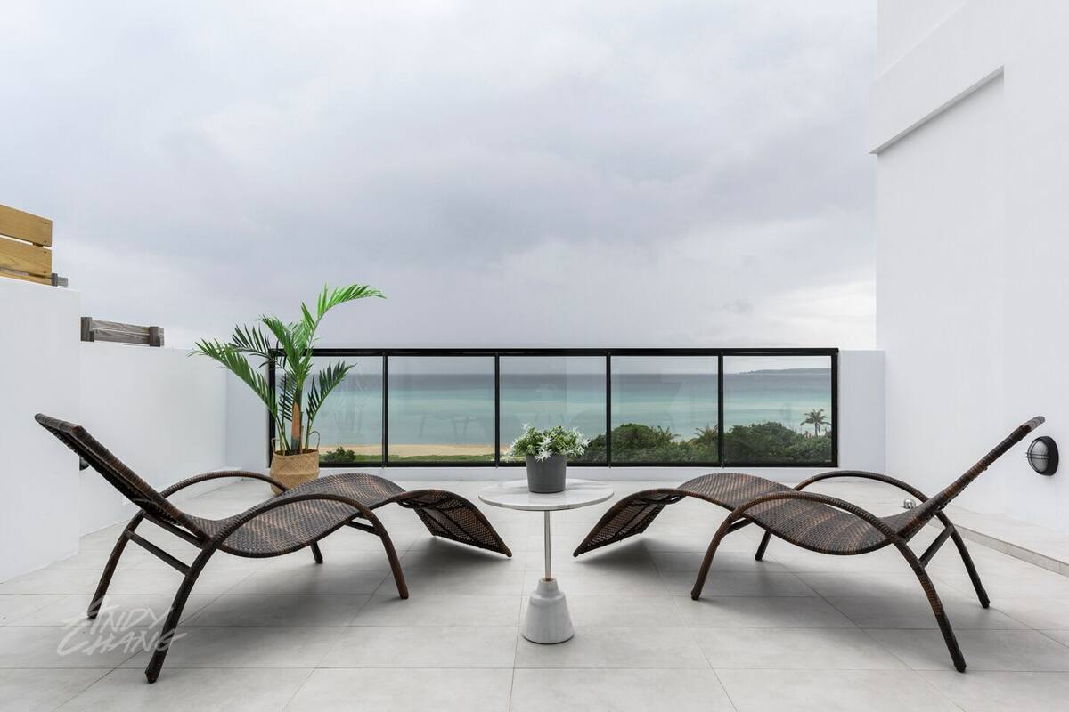Een balkon met rieten stoelen, een tafeltje en potplanten.
