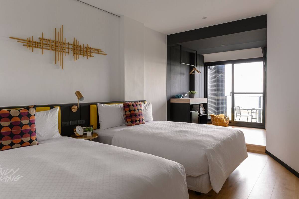 Een moderne hotelkamer met twee bedden, een kunstwerk aan de muur, een nachtkastje met een lamp en uitzicht op de omgeving.