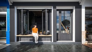 A person sitting on a bench outside a building with large glass doors and windows, a staircase, and a pool area visible in the background. - Hido Hotel I (Hengchun)