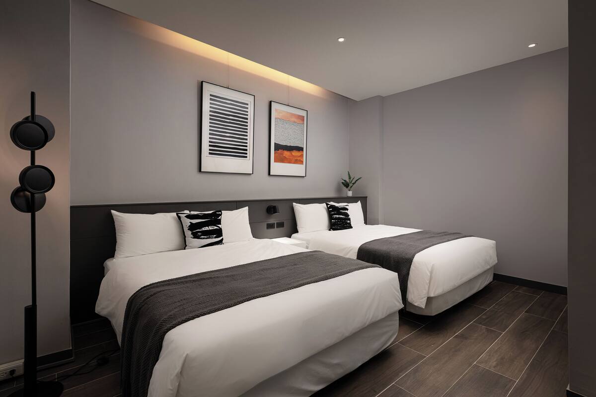 Una habitación de hotel moderna con dos camas, una lámpara de pie y obras de arte en la pared.