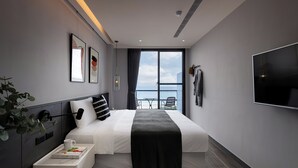 A modern hotel room with a bed, bedside table, TV, artwork, and a view of the sea. - Hido Hotel II (Hengchun)