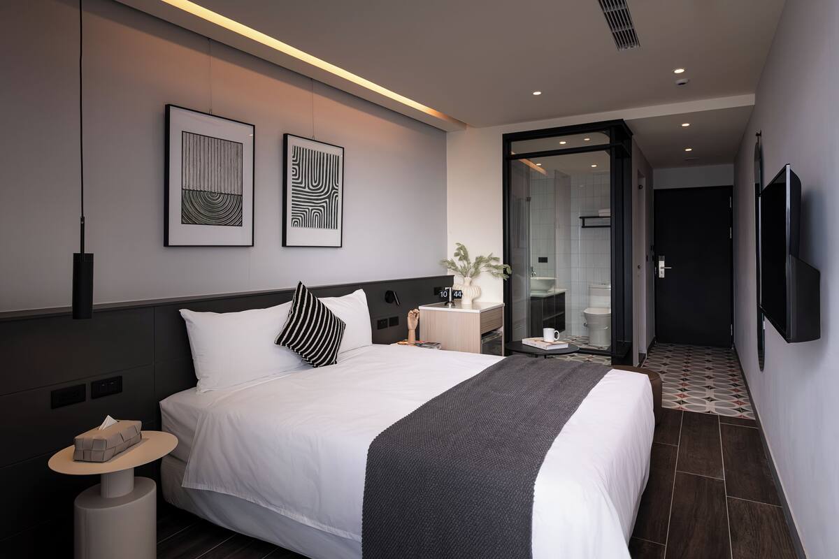 Una habitación de hotel moderna con una cama grande, mesitas de noche, un televisor y obras de arte en la pared.