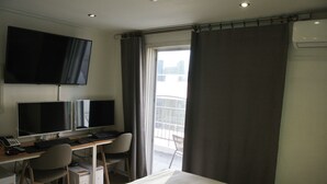 Ein Hotelzimmer mit einem Bett, einem Schreibtisch mit zwei Monitoren, einem Stuhl und einem an der Wand montierten Fernseher.