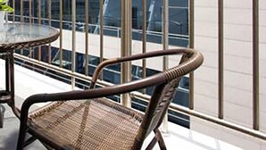 Ein Balkon mit Korbstühlen und einem Glastisch, mit Blick auf ein modernes Gebäude mit Glasfassade.