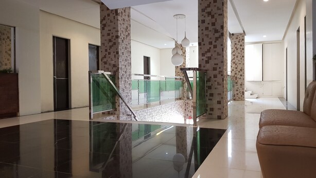 Un vestíbulo amplio con suelo pulido, una escalera con barandillas de cristal y una zona de estar con sofá.